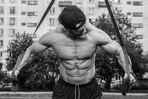 Muscular man performing a suspension training exercise outdoors, highlighting the upper body strength developed through the deficit push-up.