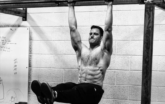 Man performing a hanging leg raise exercise in a gym, demonstrating how to stay consistent with exercise through focused daily practice.