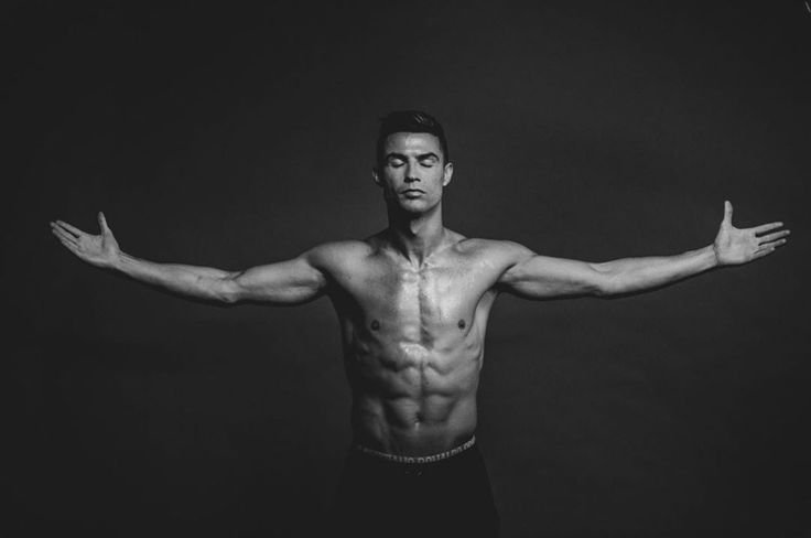 Monochrome image of a fit, shirtless man standing with arms outstretched, embodying strength and focus, representing workout consistency.