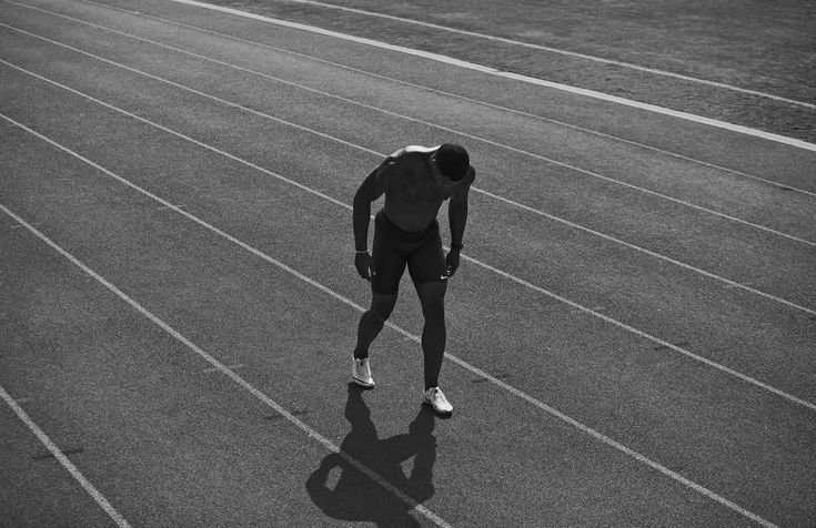 A lone athlete on a track, bent over in exhaustion, symbolizing the humility and dedication needed to achieve long-term fitness goals.