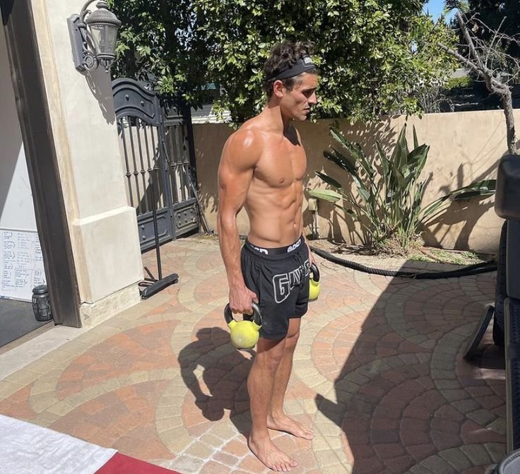 Shirtless man in backyard holding kettlebell, illustrating importance of spinal rotation in fitness.