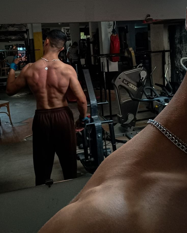 Back view of a muscular man in a gym, highlighting his defined back and arm muscles, showcasing the results of a calisthenics workout plan for beginners.