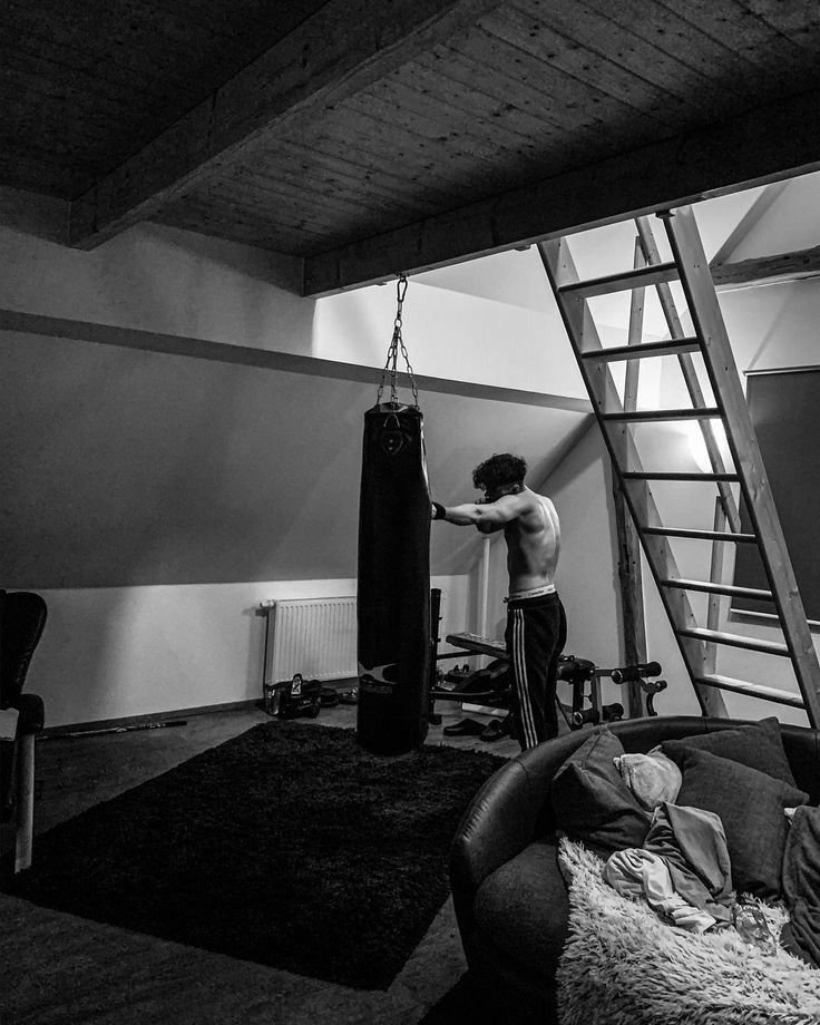 Man in a home gym focusing on a heavy punching bag, highlighting the importance of quality over quantity in exercise with a minimalist, dedicated workout space.