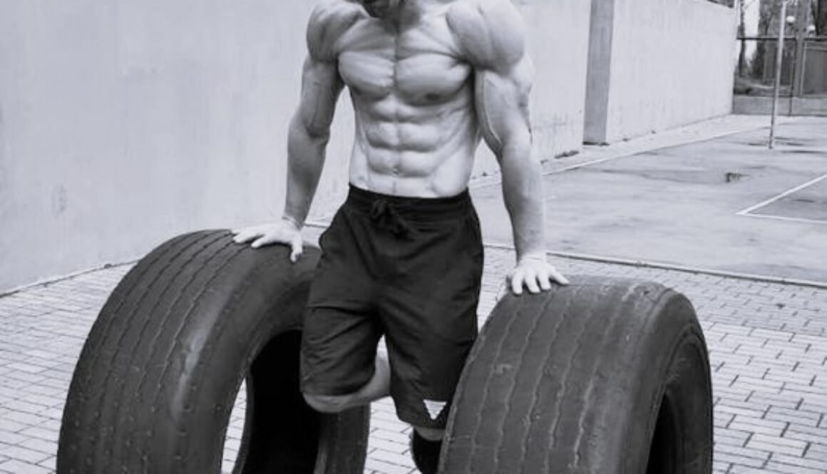 Muscular man performing calisthenics exercise with large tires, demonstrating the principle of quality over quantity in exercise through focused, controlled movements.