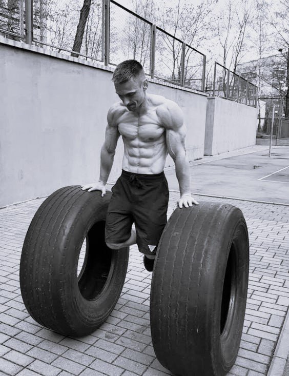 Muscular man performing calisthenics exercise with large tires, demonstrating the principle of quality over quantity in exercise through focused, controlled movements.